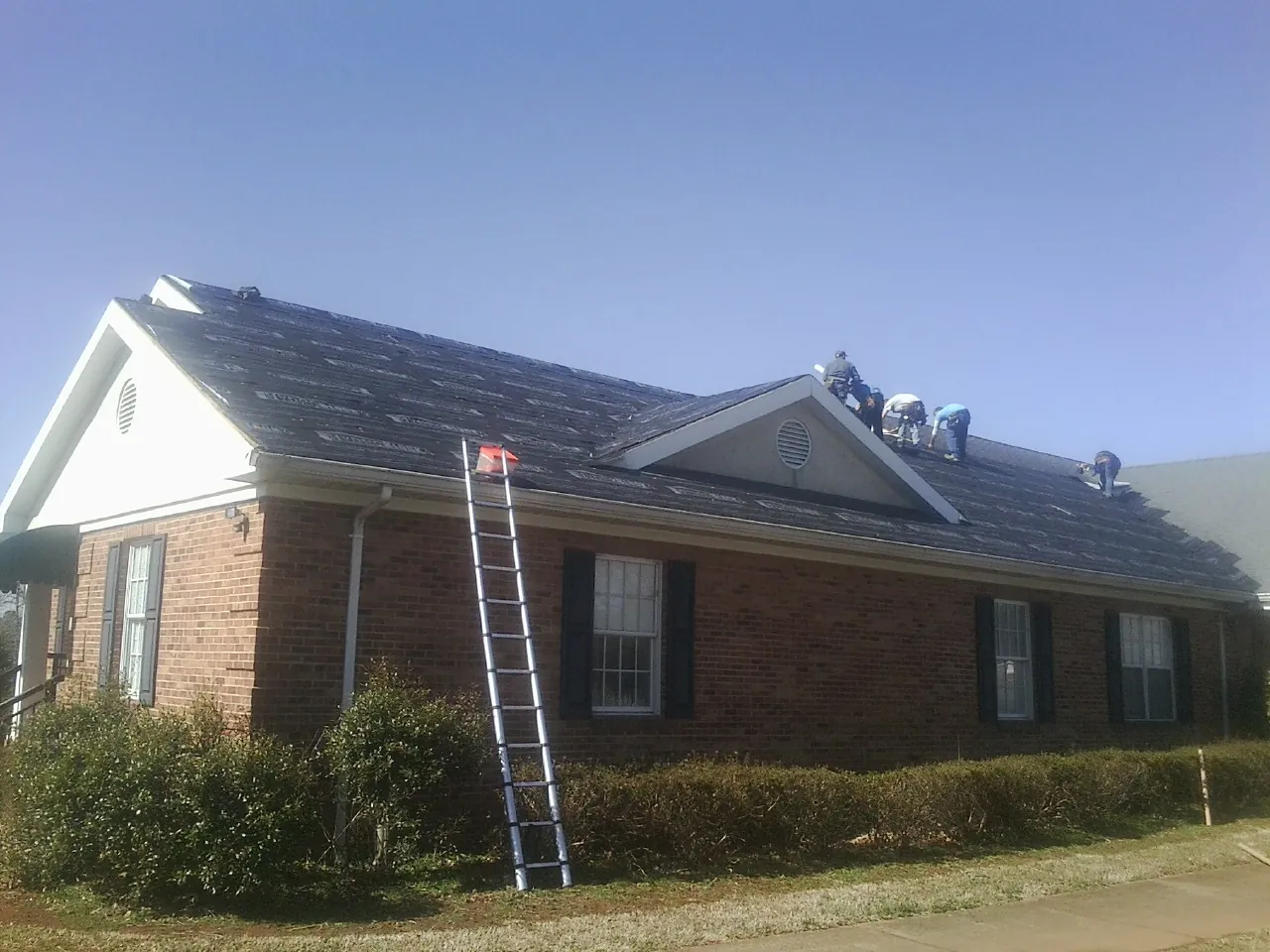 Crew tearing shingles off a brick ranch roof with a ladder set — Emergency Roof Repair work by our crew in Bern