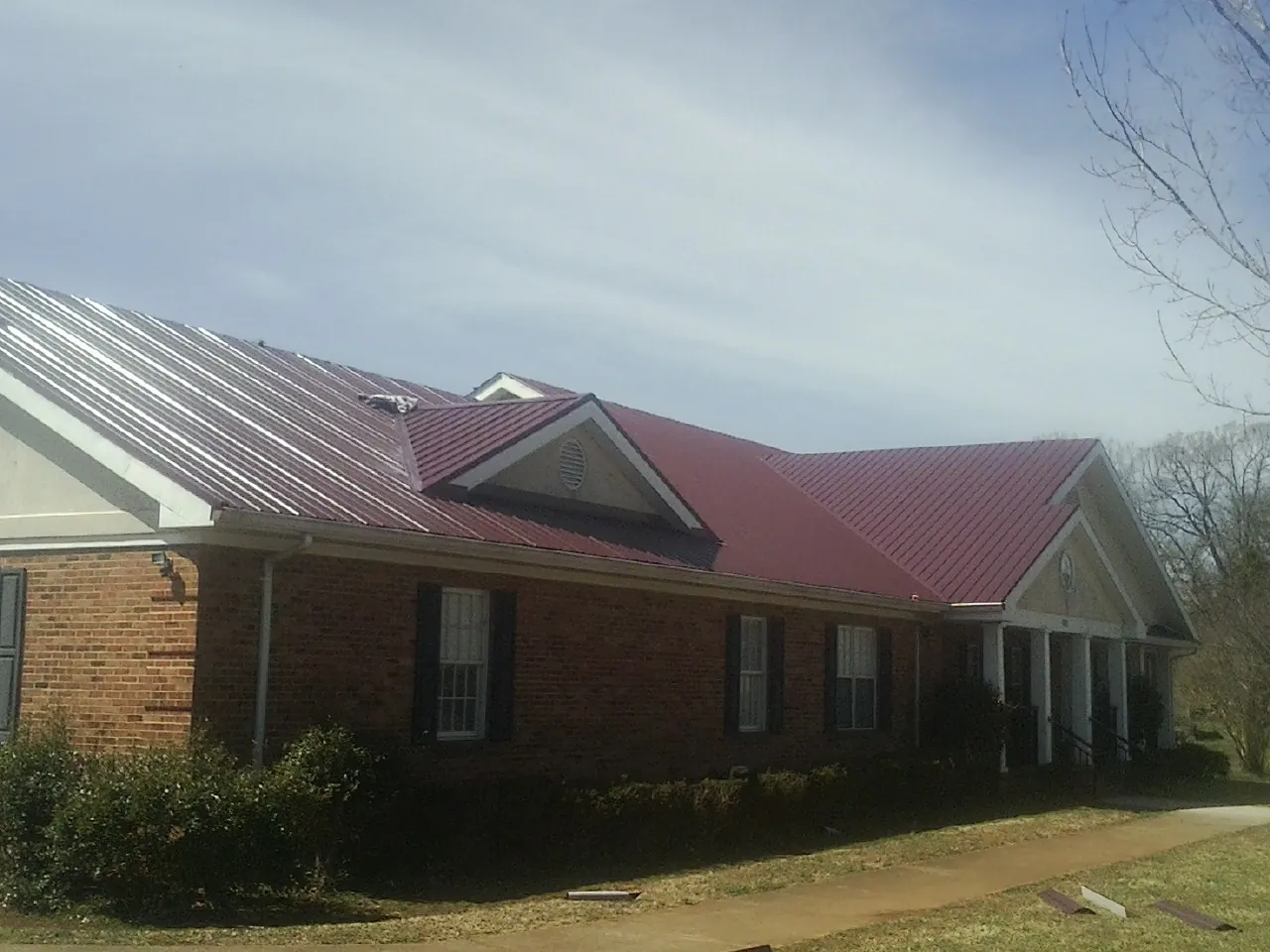 Red metal roof with gabled entries on a long brick building, from a Hail Damage Roof Repair job in Bern