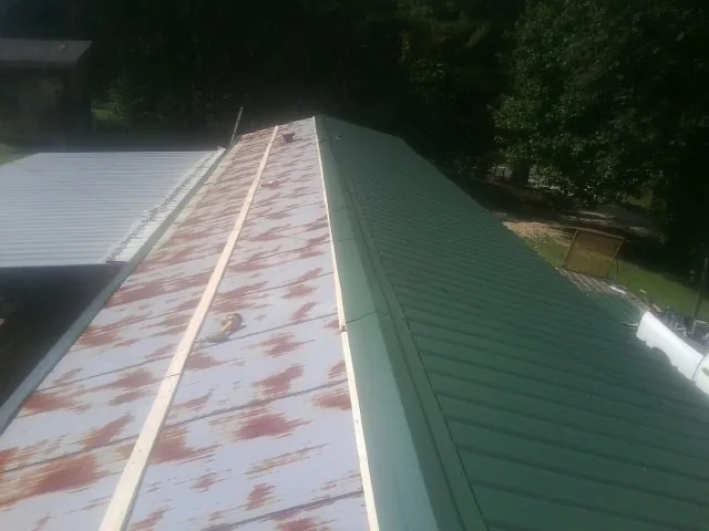 Old rusted panels beside newly installed green metal roofing — Wind Damage Roof Repair by Roofing Brothers in Bern