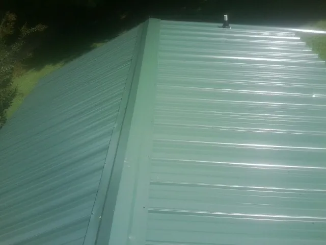New green metal panels meeting at the ridge of a roof — Flat Roof Repair work by our crew in Bern