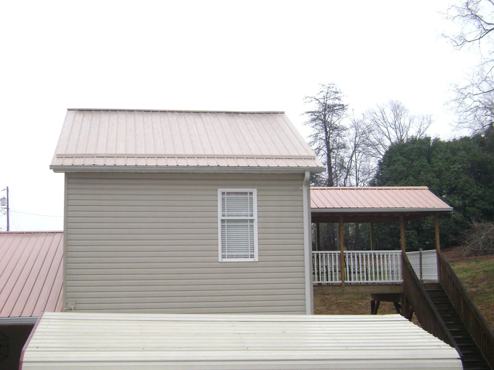 Tan metal roofs on a two story addition and attached porch, from a Roof Replacement job in Bern